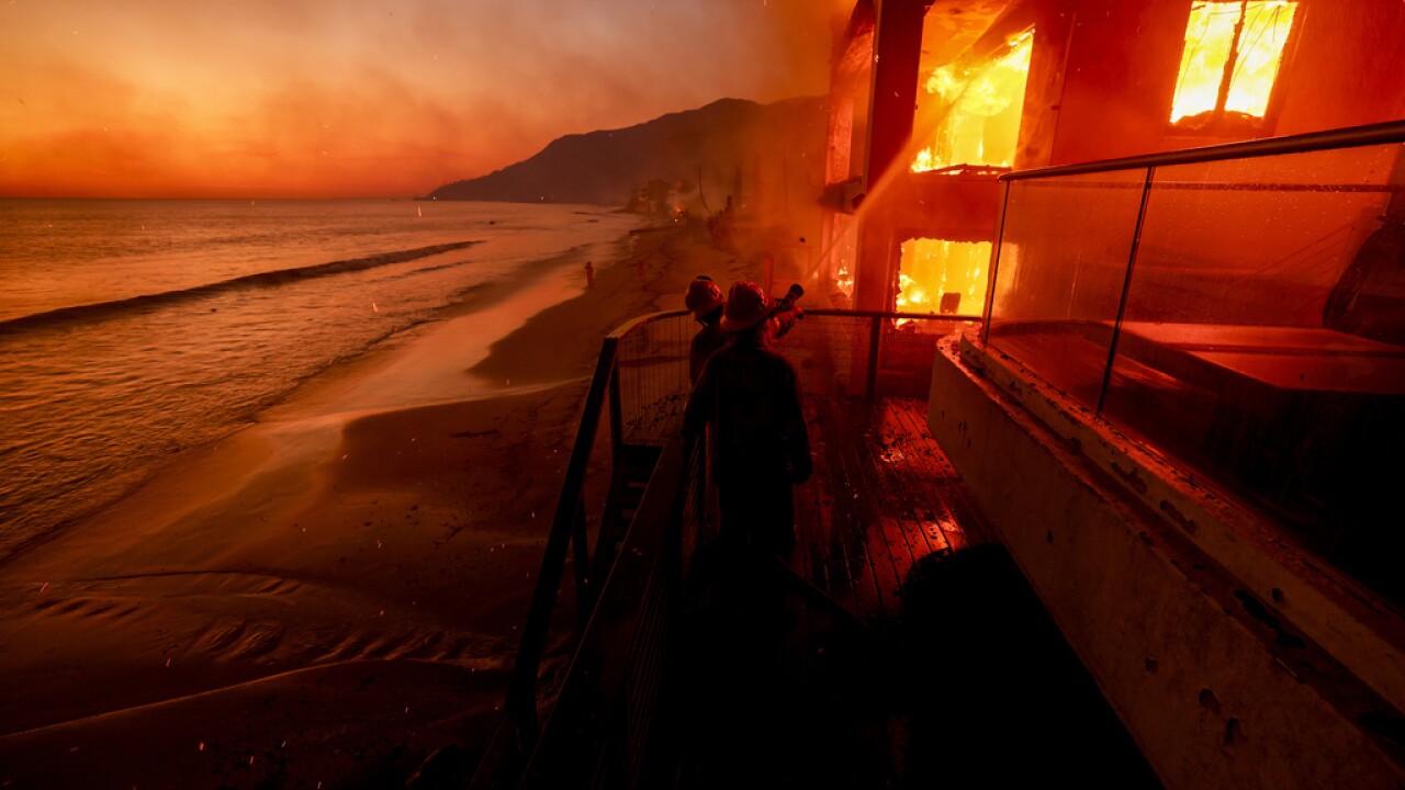 Firefighters work from a deck as the Palisades Fire burns